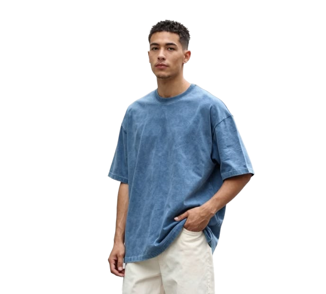 Young man wearing a loose-fitting blue short-sleeve t-shirt and light-colored pants with one hand in his pocket.