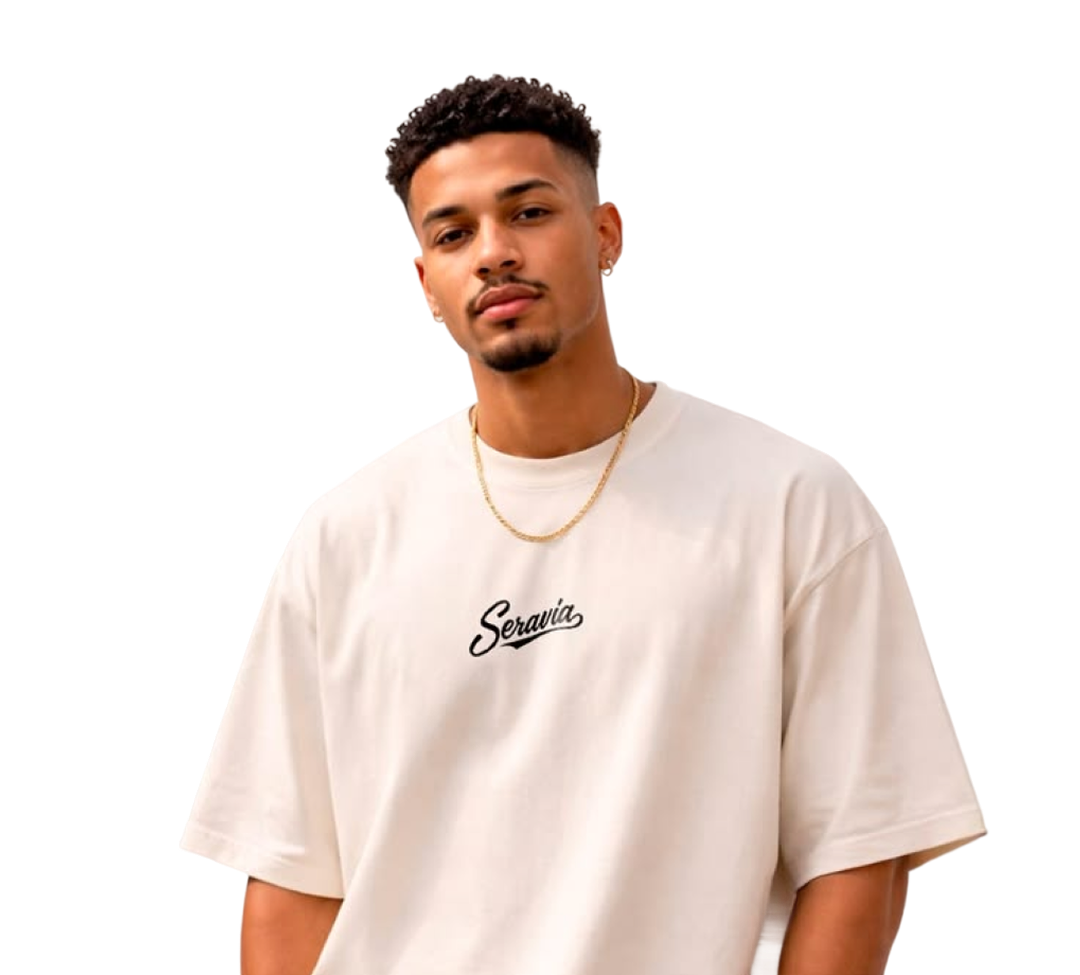 Young man with short curly hair and beard wearing a white Seravia t-shirt and a gold chain necklace.