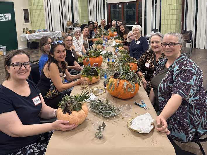 Group of women seated around a long table making decorative succulent pumpkin arrangements.
