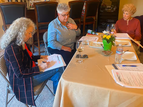 Three women sitting around a table with documents, writing and talking in a meeting.