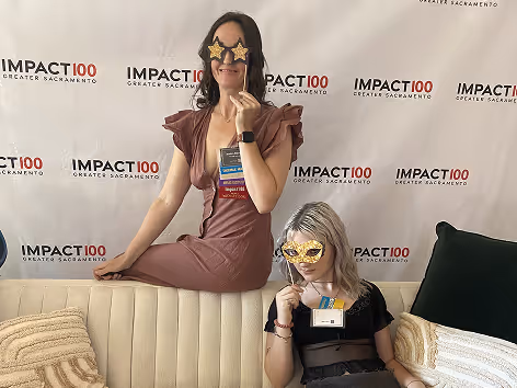Two women at an Impact100 Greater Sacramento event holding star-shaped masks in front of their faces.