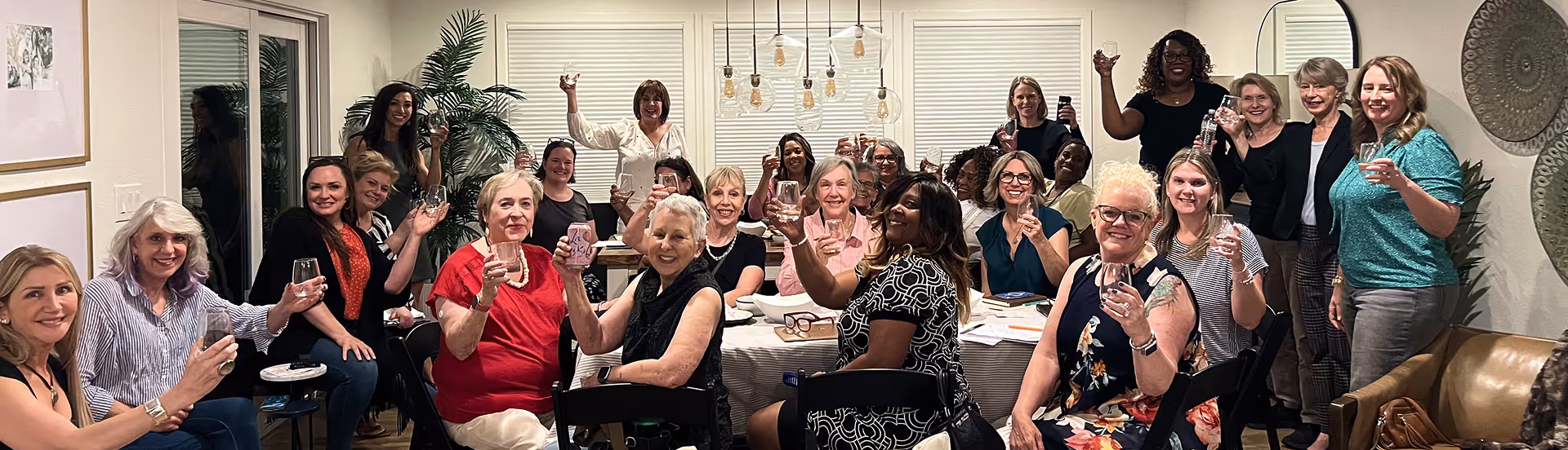 Group of diverse women smiling and raising glasses for a toast in a cozy indoor gathering.