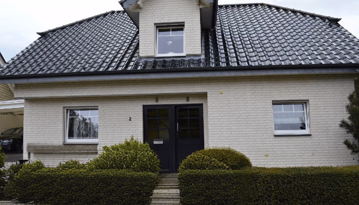 Einfamilienhaus mit weißer Backsteinfassade, dunklem Dach und gepflegtem Vorgarten.