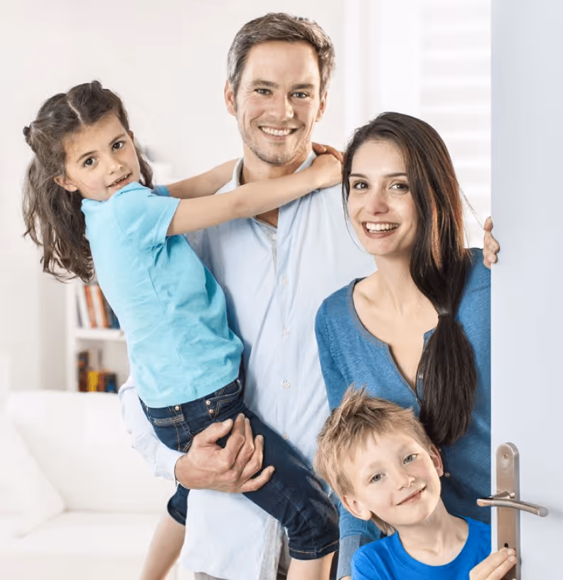 Lächelnde Familie steht in Tür, Eltern mit zwei Kindern, alle in blauer Kleidung, Wohnzimmer im Hintergrund.