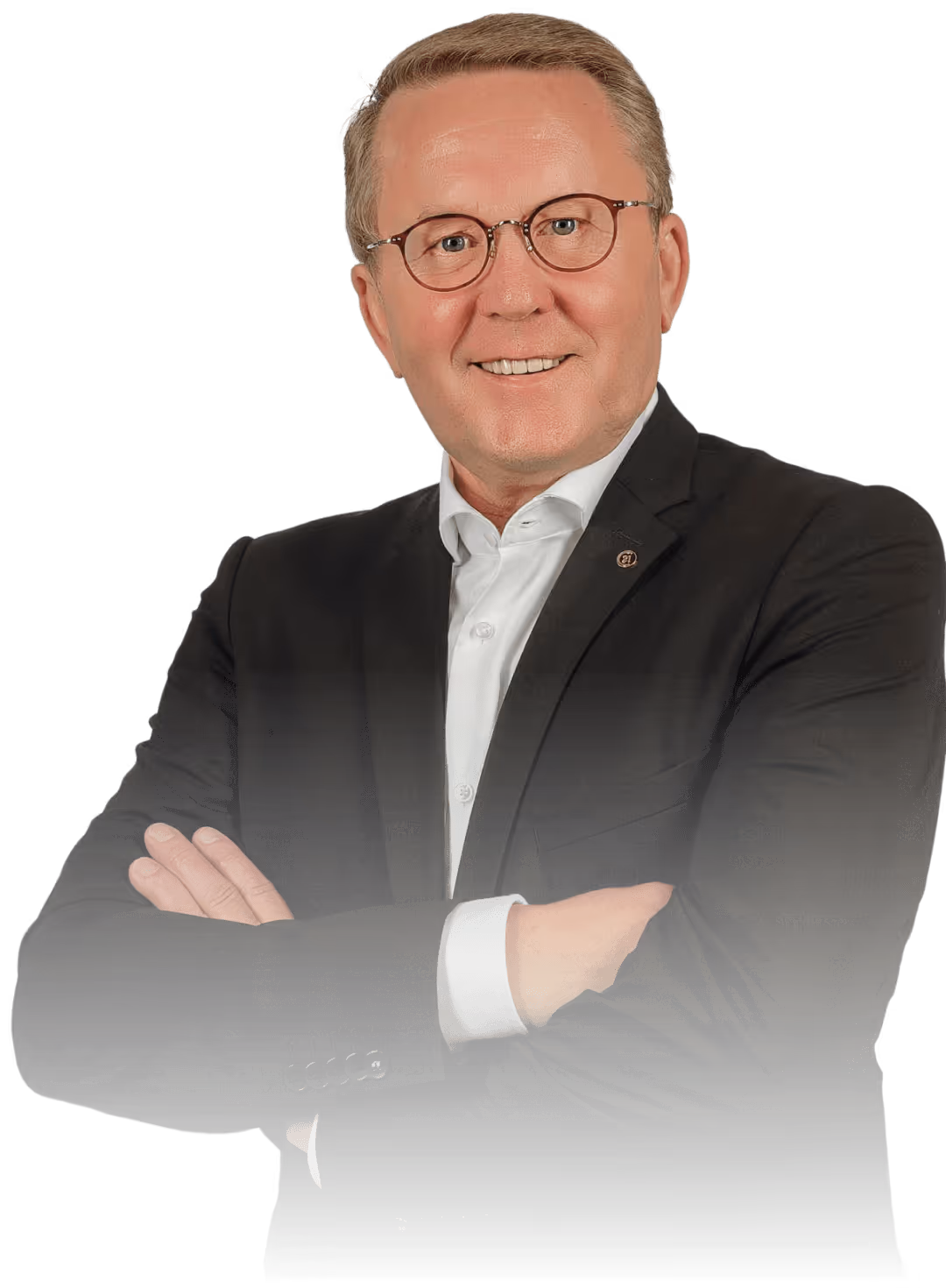 Mann in dunklem Anzug und Brille lächelt mit verschränkten Armen vor schwarzem Hintergrund.