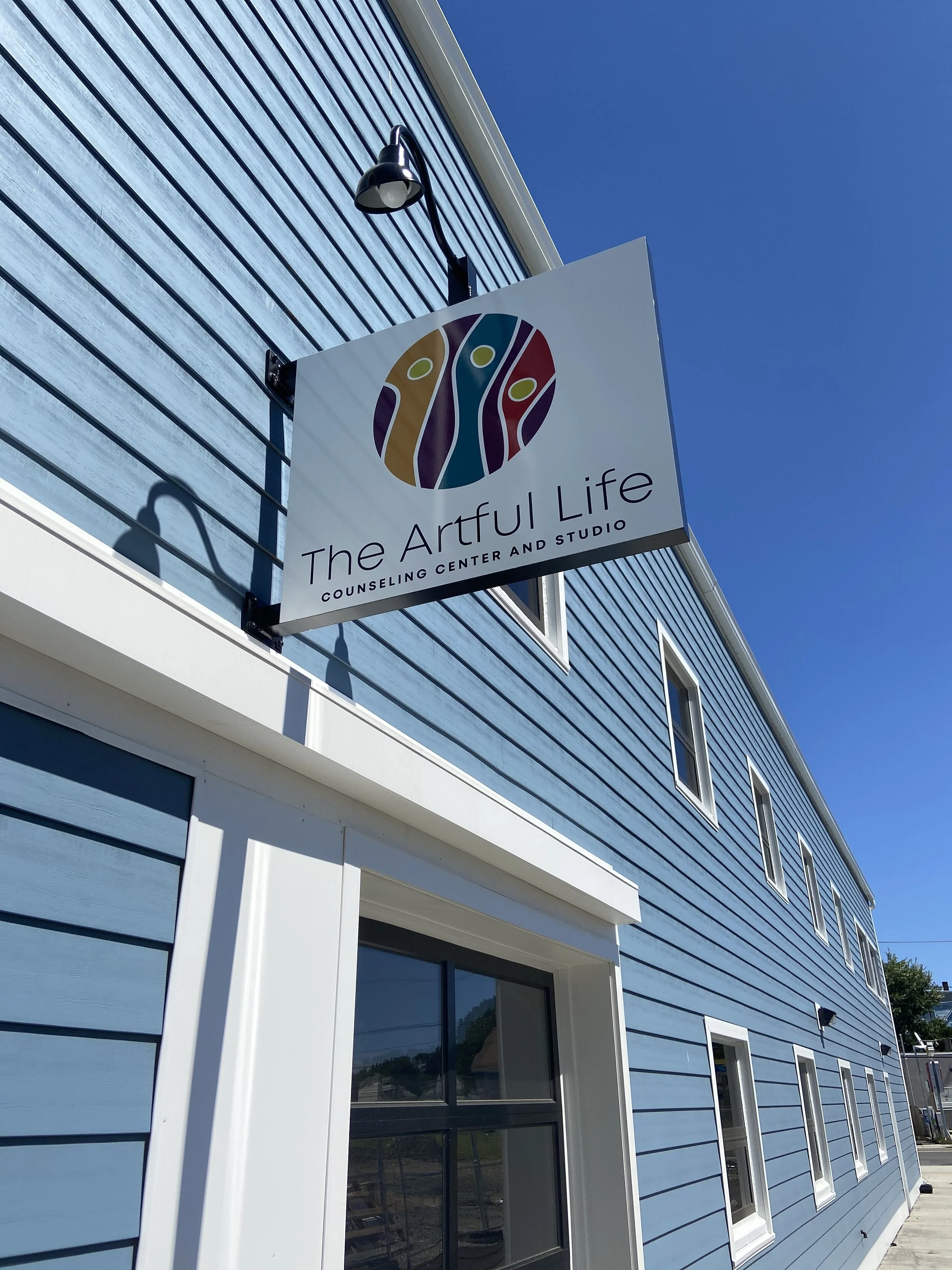 Sign for The Artful Life counseling center mounted on a blue building under a clear sky.