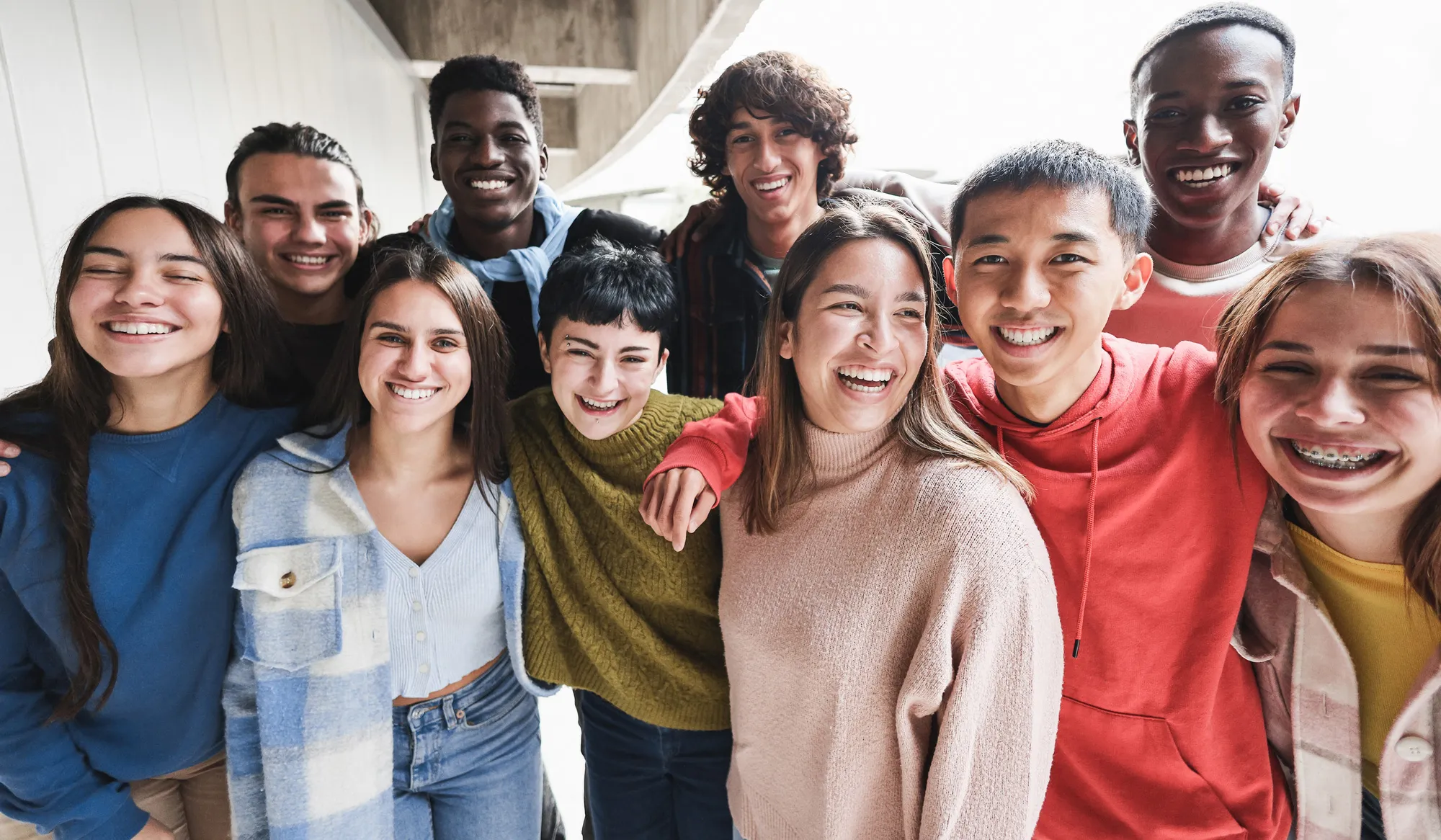 Group of diverse teens smiling and posing with arms around each other in a bright setting.