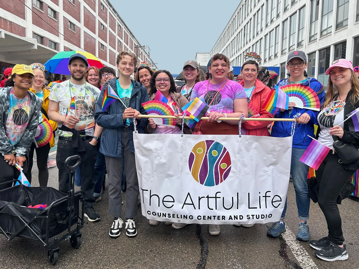 Group holding pride flags and banner for The Artful Life Counseling Center and Studio at an outdoor event.