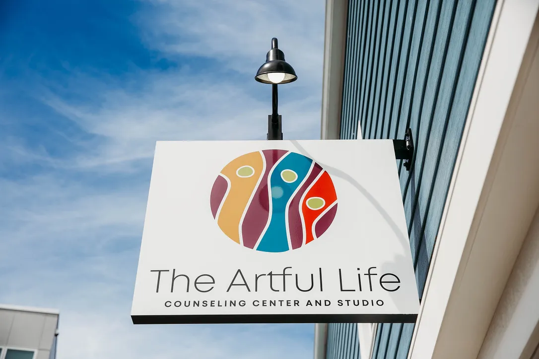 Outdoor sign for The Artful Life counseling center with colorful abstract logo on white background.