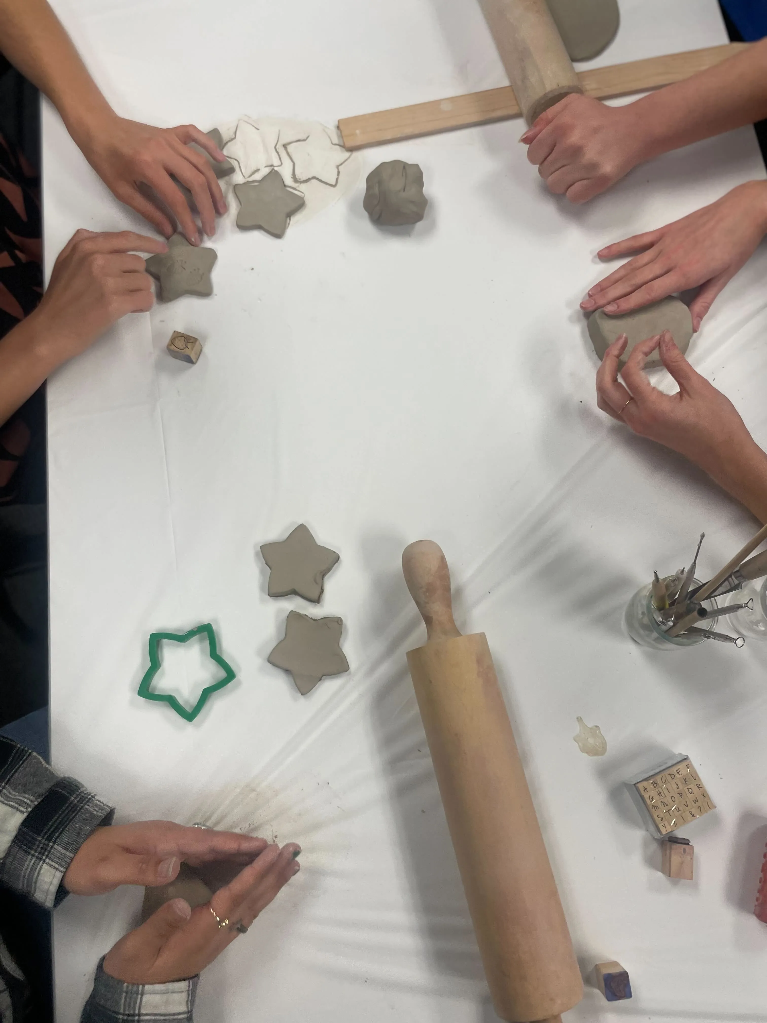 Hands shaping and stamping clay stars on a white table with a rolling pin and sculpting tools.