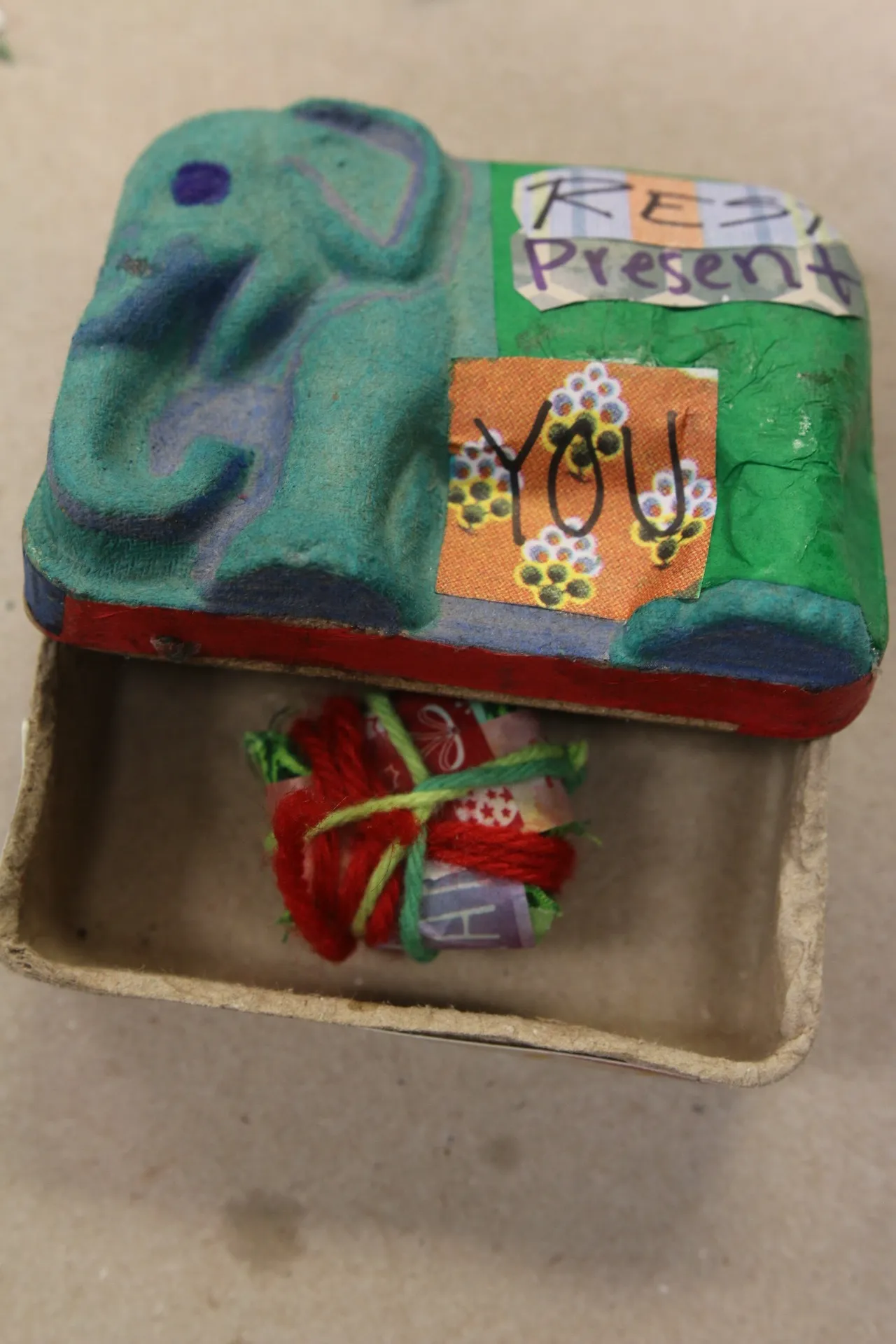 Small green elephant-shaped box with 'You' and 'Present' labels, open with yarn inside.