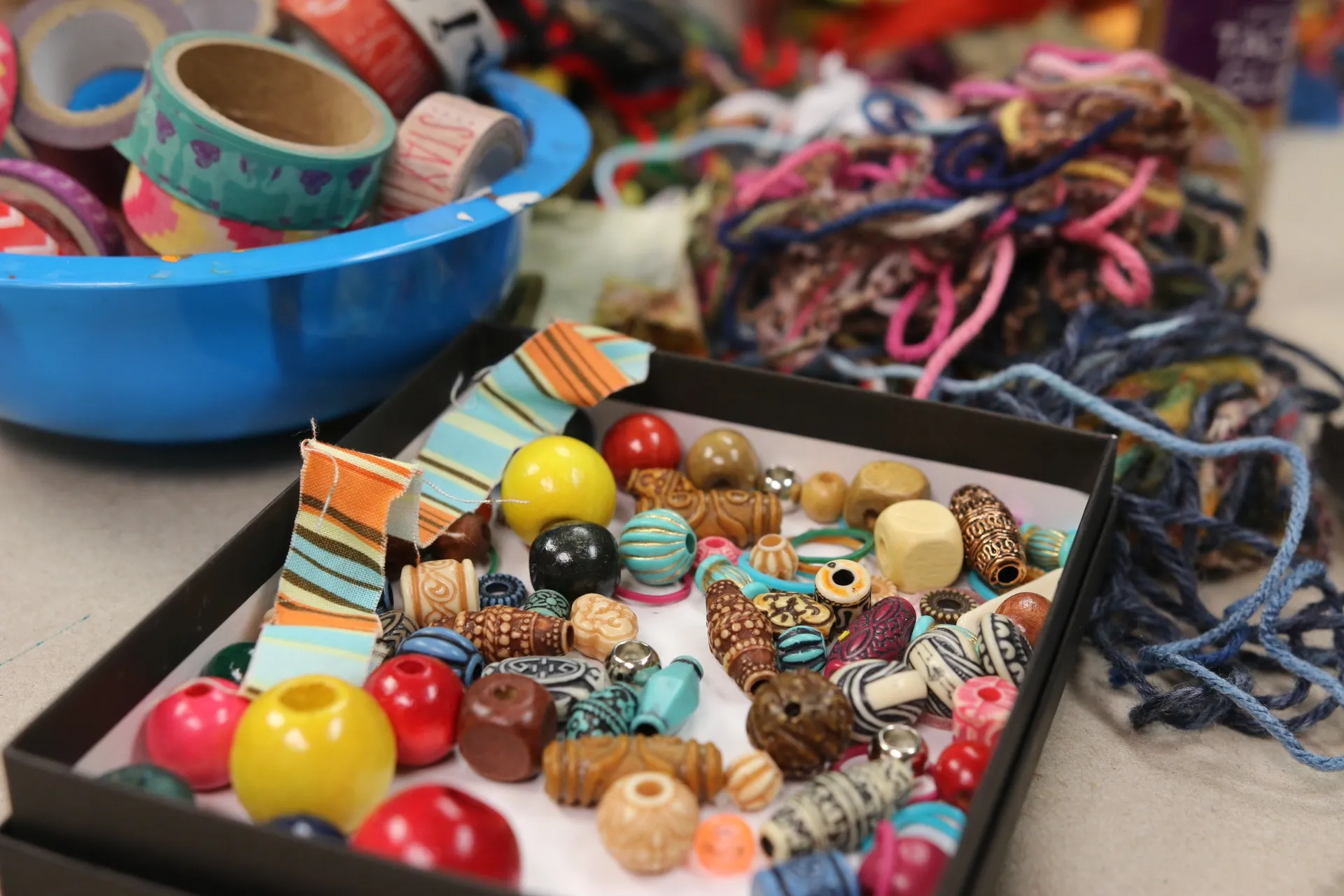 Colorful assorted beads, patterned ribbons, and yarn for crafting on a table.