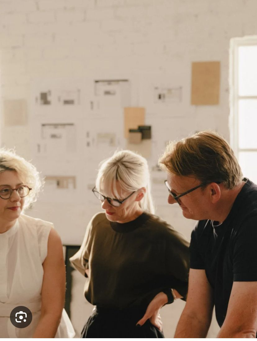 Three adults wearing glasses engaged in conversation inside a room