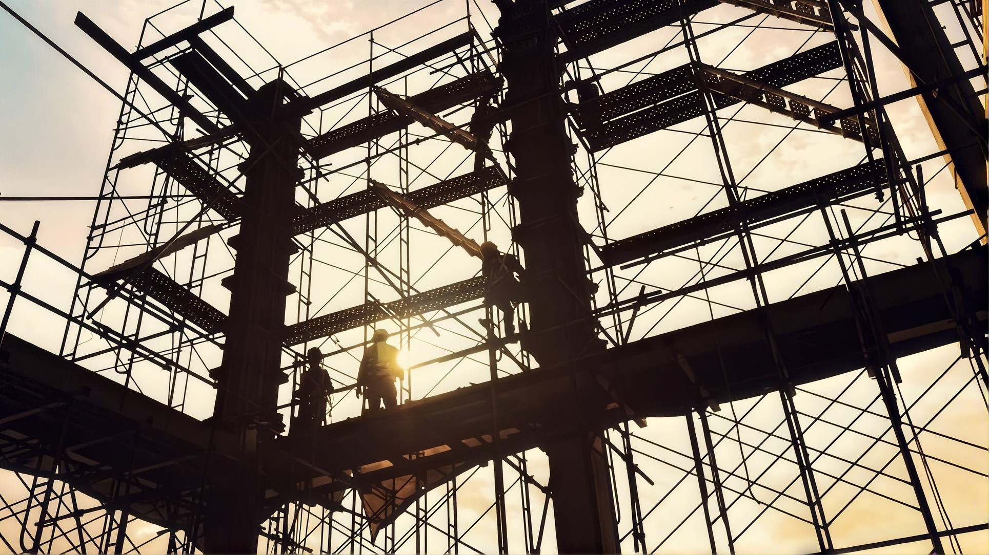 Silhouettes of construction workers wearing helmets on scaffolding at a building site