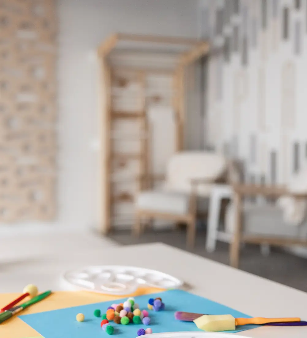 Art therapy table set up for a kids counselor session with paint palette, pom-poms, and brushes at Playful Pathways