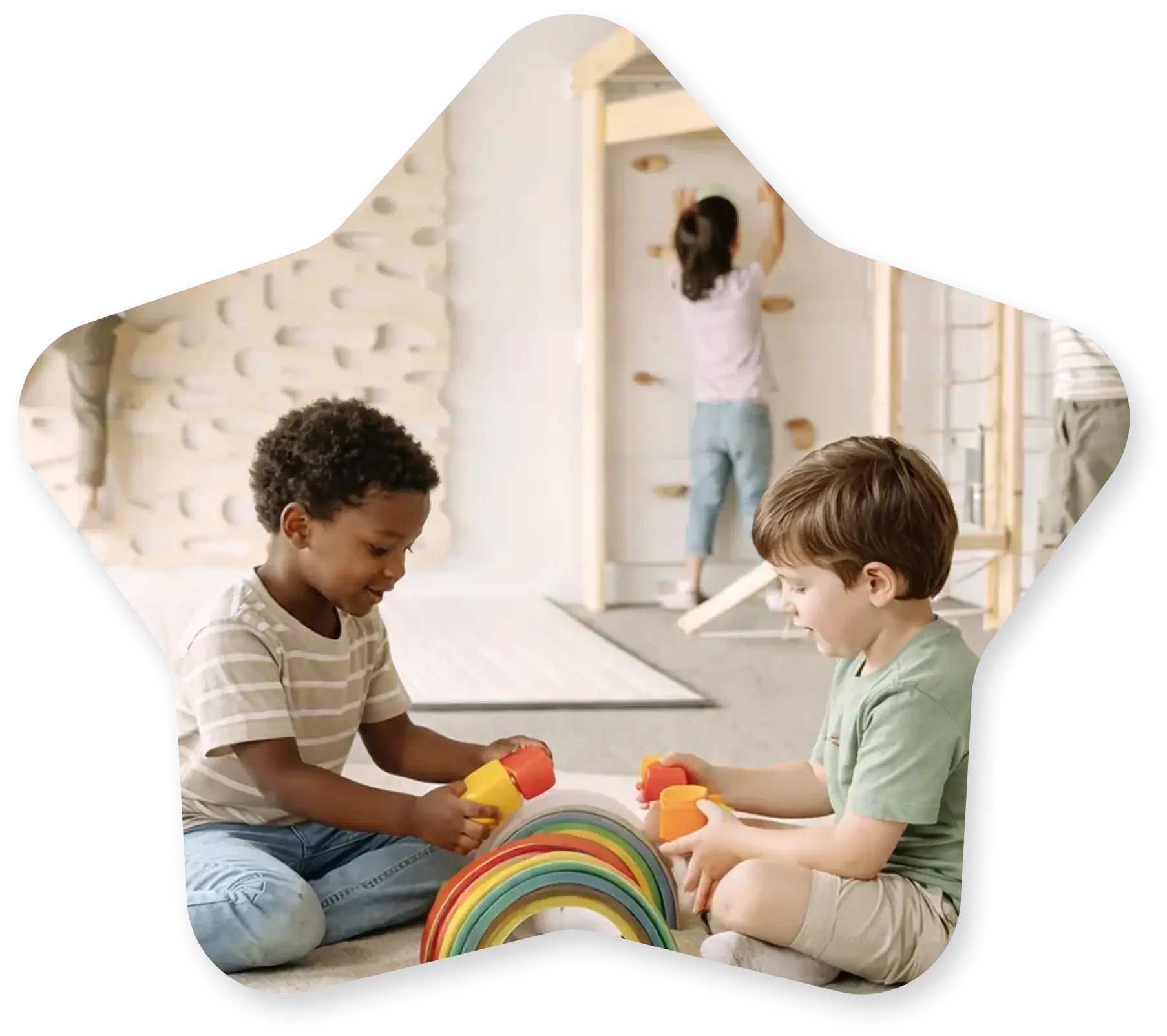 Kids in a play therapy session using a wooden rainbow stacker while another child climbs the rock wall at Playful Pathways