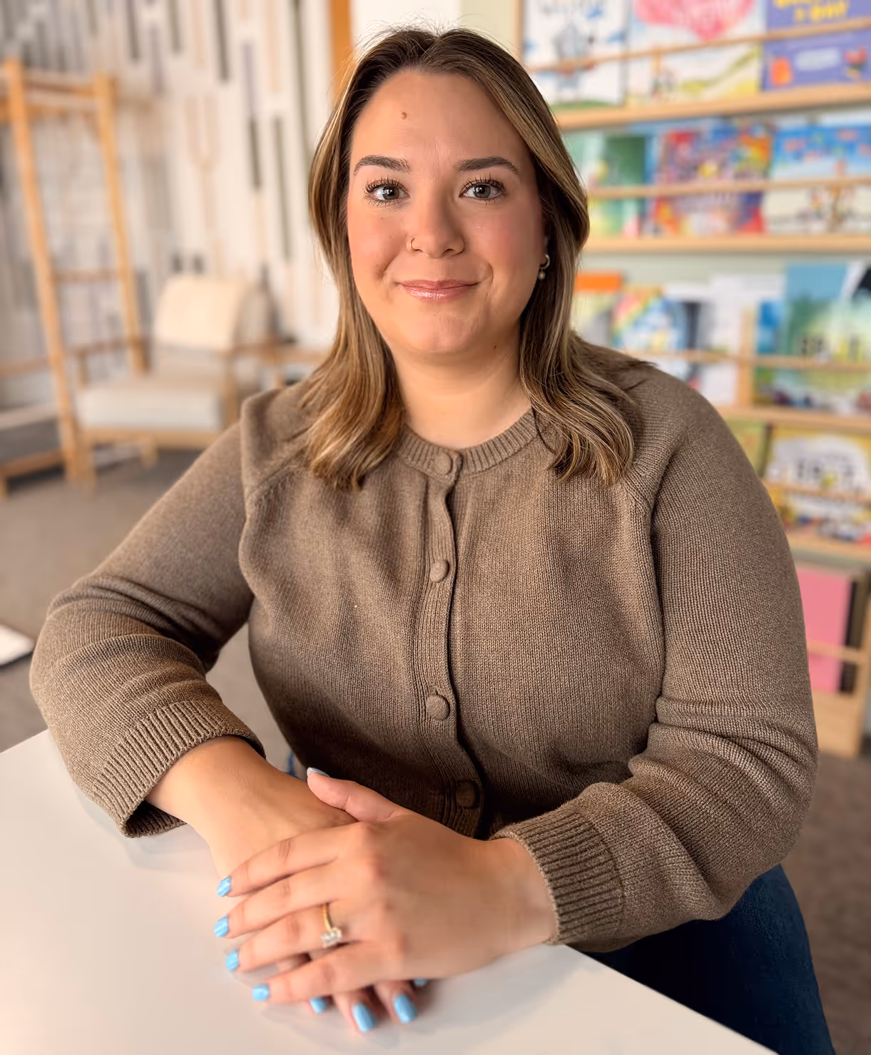 Kids elementary tutor at Playful Pathways in Berkley Michigan, smiling at the work table with a children's book display behind her
