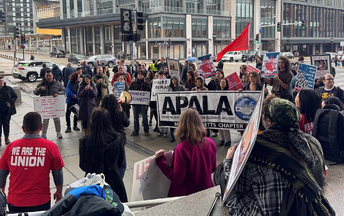 Protesters on a city sidewalk hold a banner for APALA Massachusetts and signs supporting fishers’ labor rights, including messages about solidarity and fair pay. One person speaks through a megaphone while others carry handmade placards in English and another language.