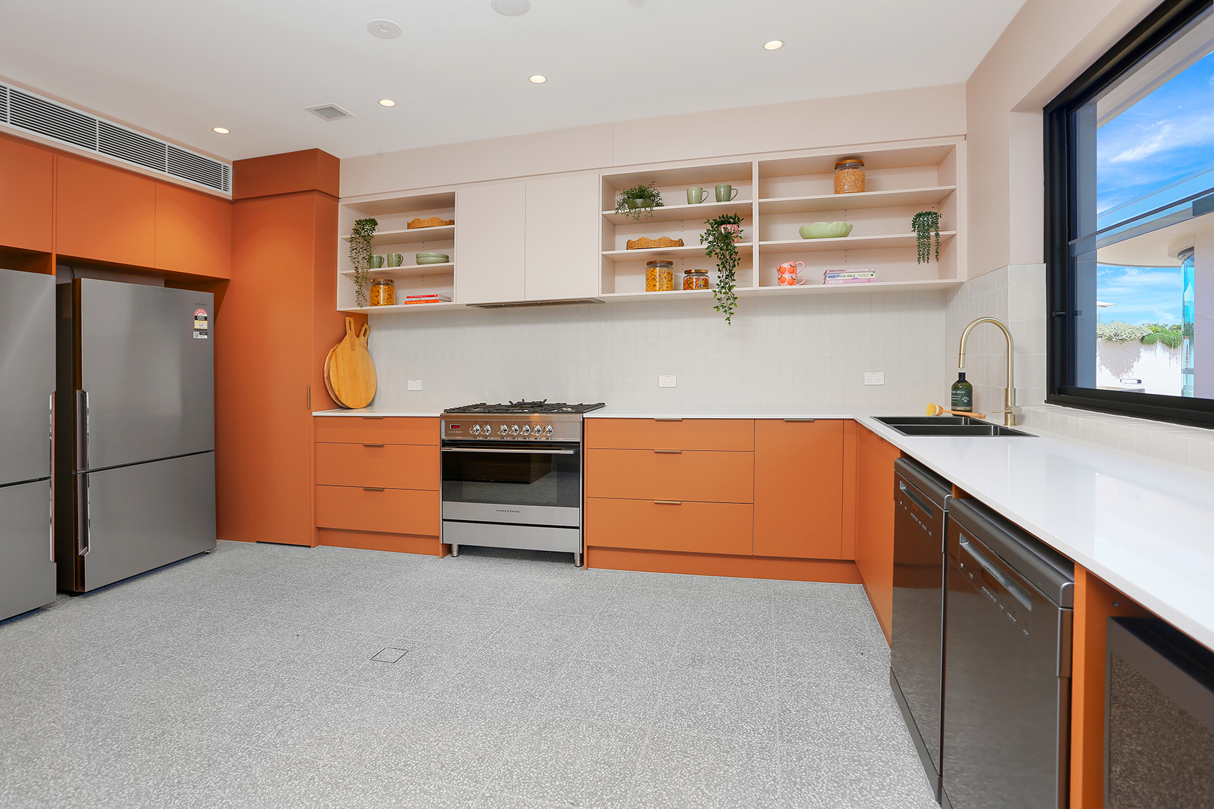SOMAs modern kitchen with orange cabinets, stainless steel appliances, white countertops, open shelves, and a window.