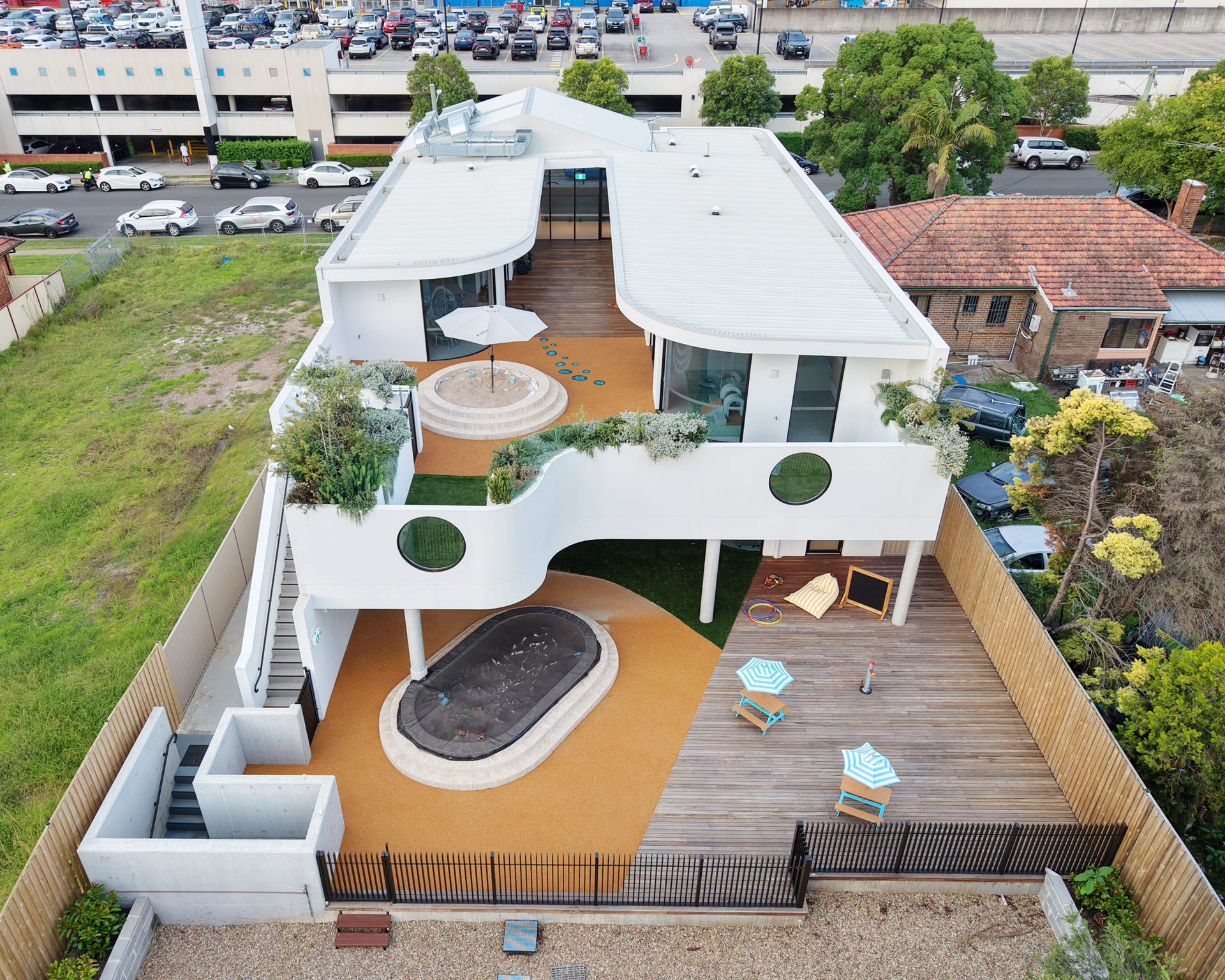 Modern two-story house with curved white facade, rooftop garden, pool, and outdoor seating area.