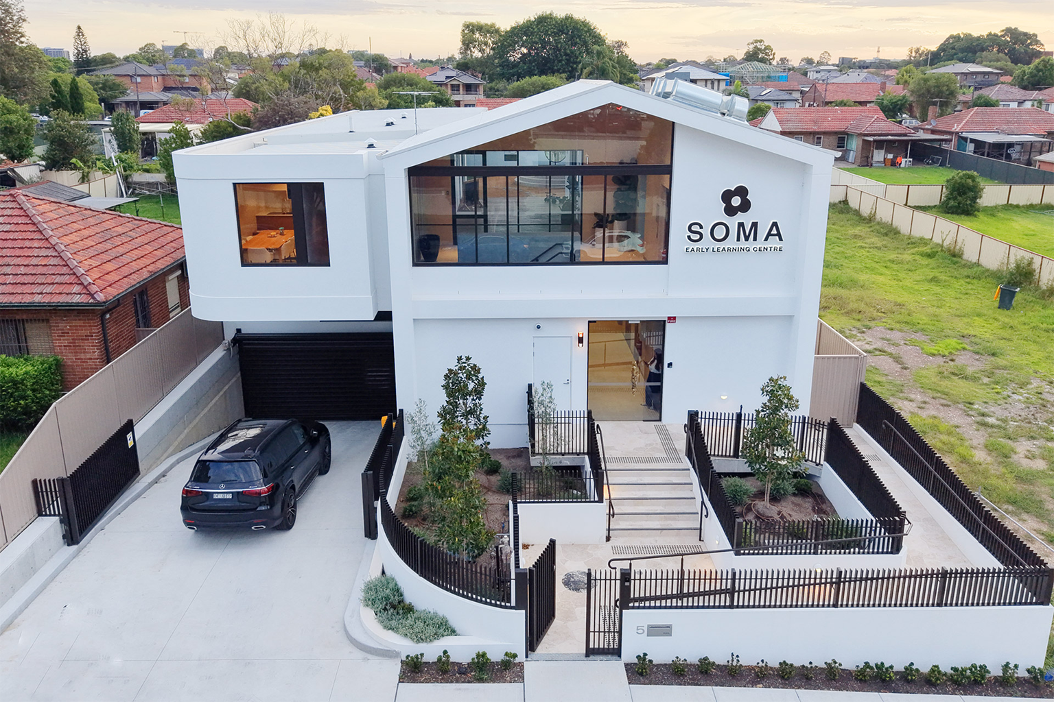 Modern white building labeled SOMA Early Learning Centre with a black car parked outside.