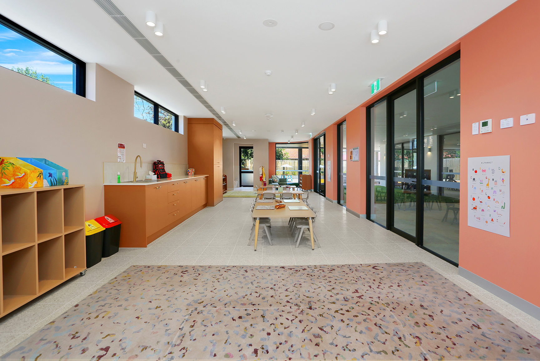 Bright, spacious classroom with tables, chairs, carpet, storage cubbies, and large windows.