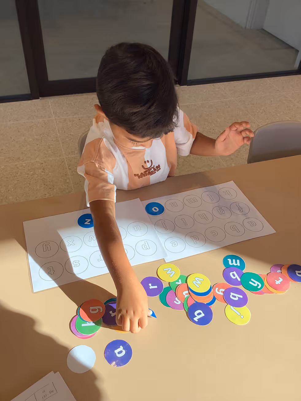 Child arranging colorful alphabet letter circles on table with alphabet worksheet.