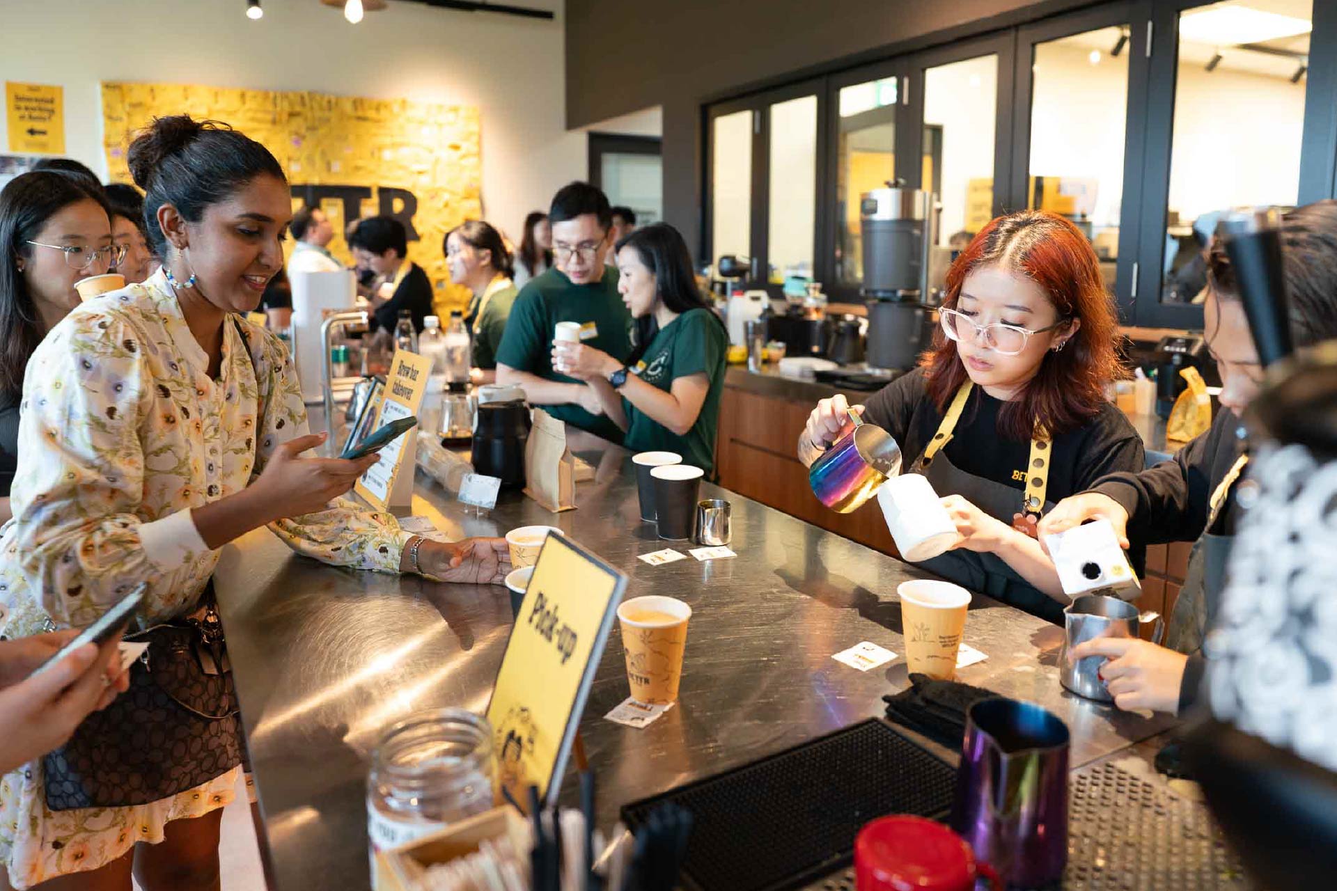 Baristas preparing coffee behind a counter with customers ordering and waiting at a cafe.