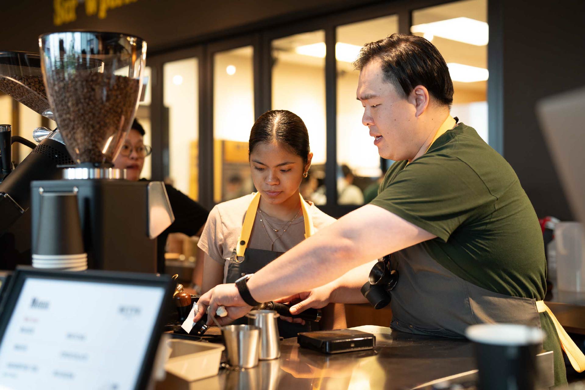 Barista teaching a woman how to use espresso machine in a coffee shop.
