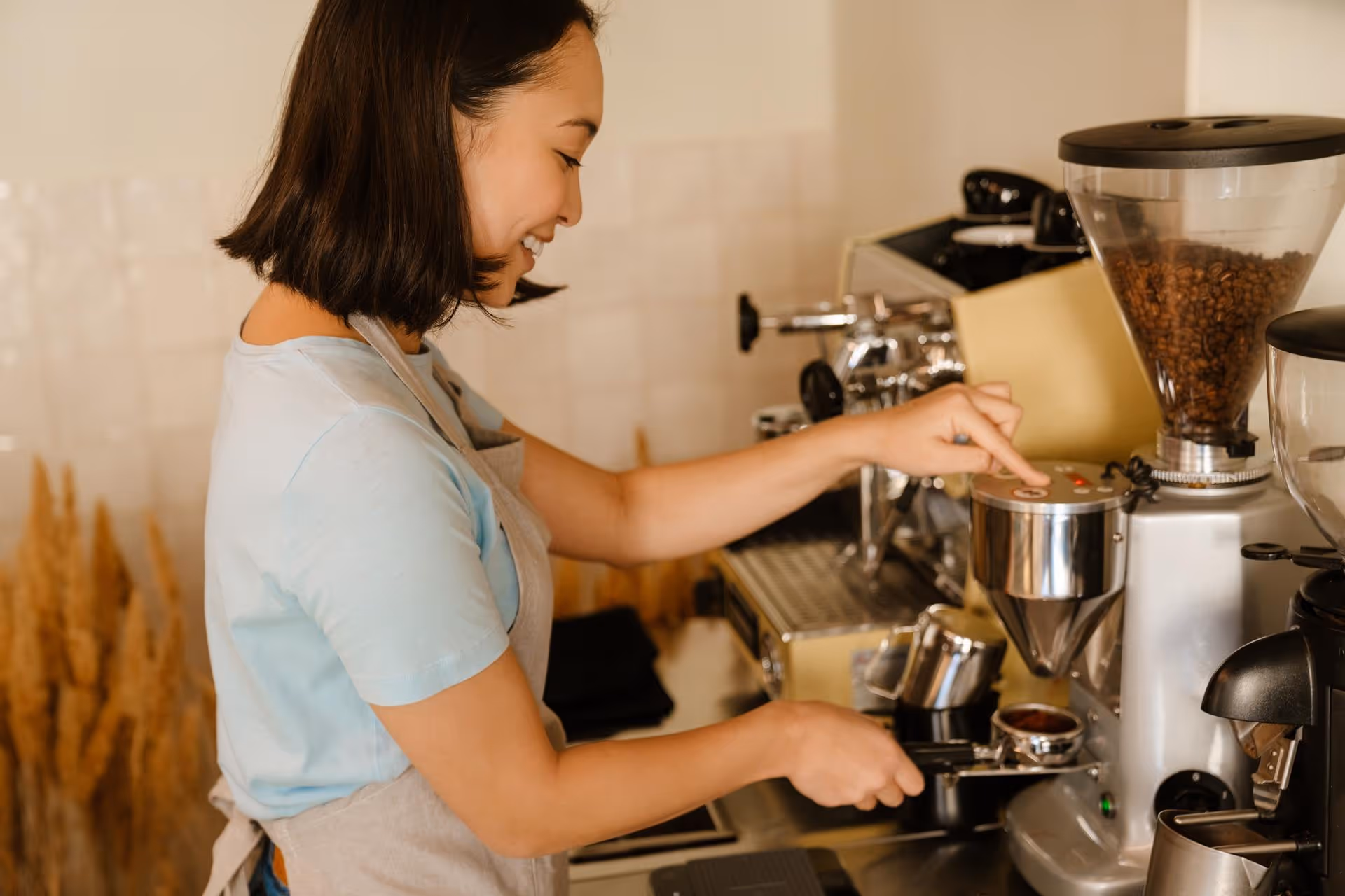 Smiling barista grinding coffee beans using a coffee grinder in a cafe setting.