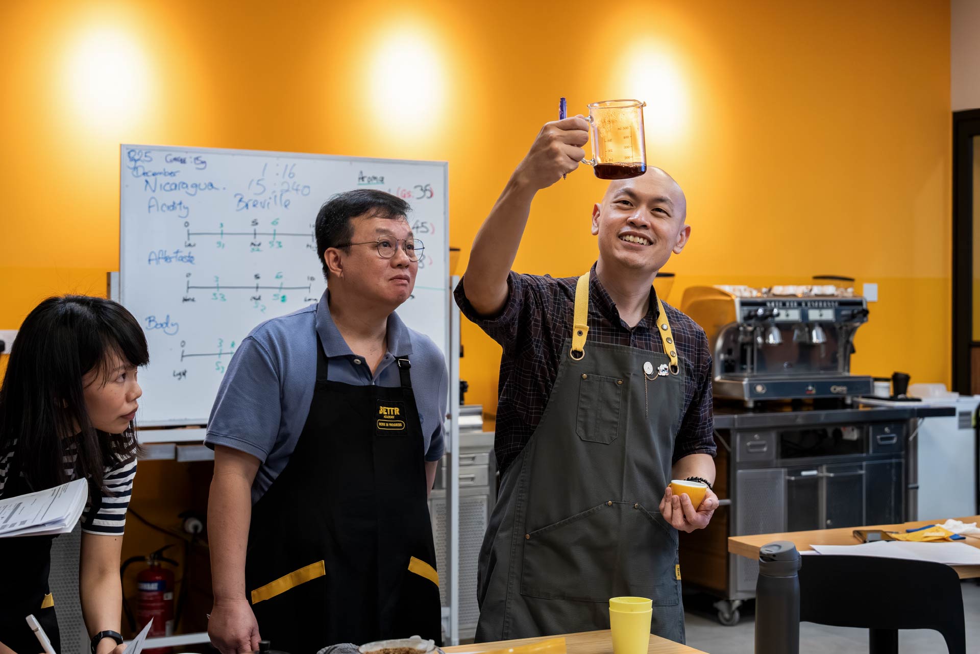 Trainer holding up a carafe of coffee and showing students next to him.