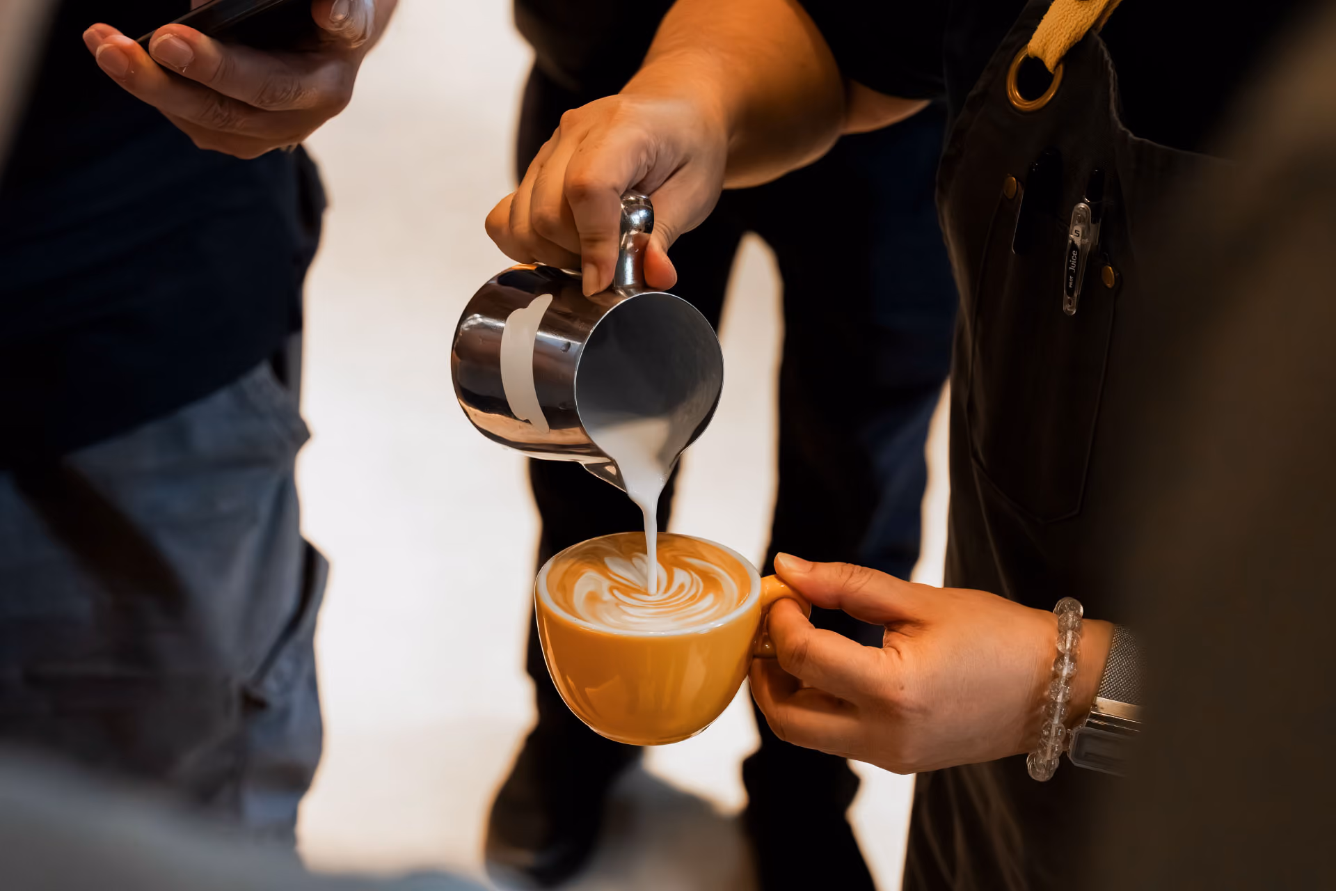 Hands holding spoons, tasting multiple cups of black coffee on a metal table.