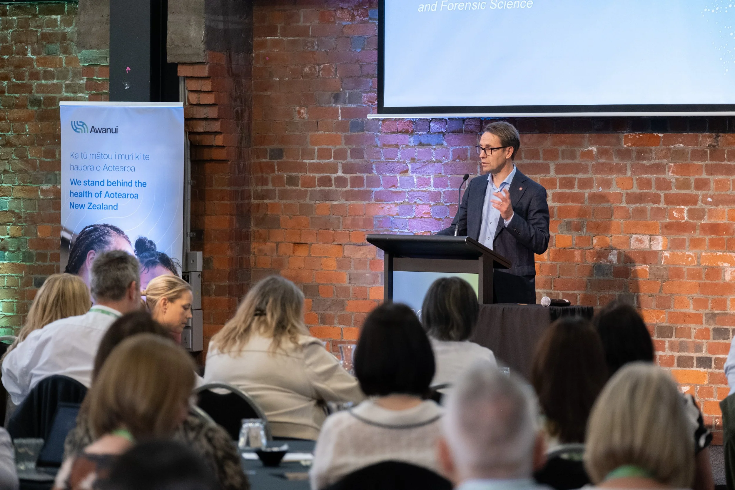A speaker presenting to the seated audience at the Co:Lab event