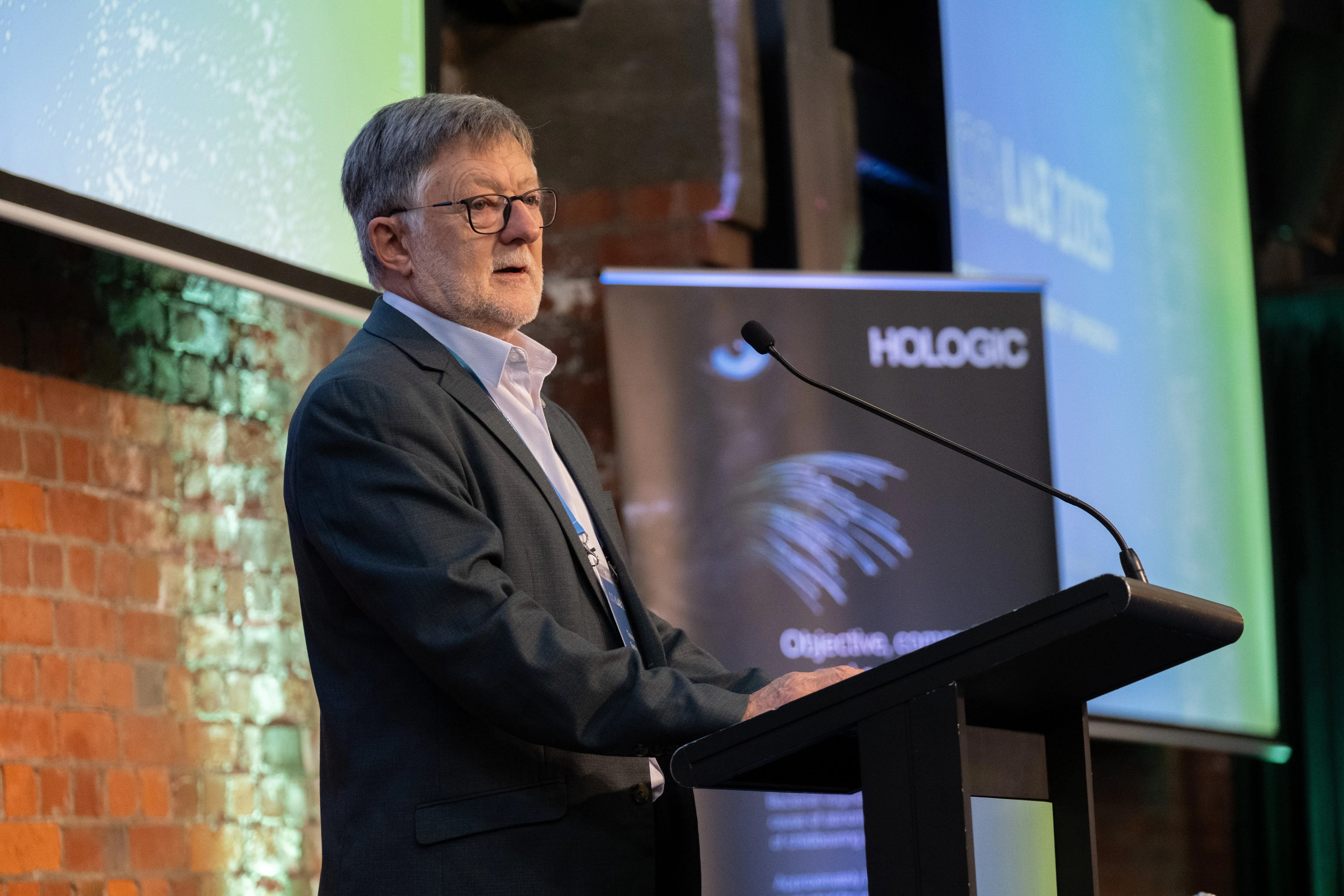 A speaker presenting at the Co:Lab podium with a Hologic banner visible