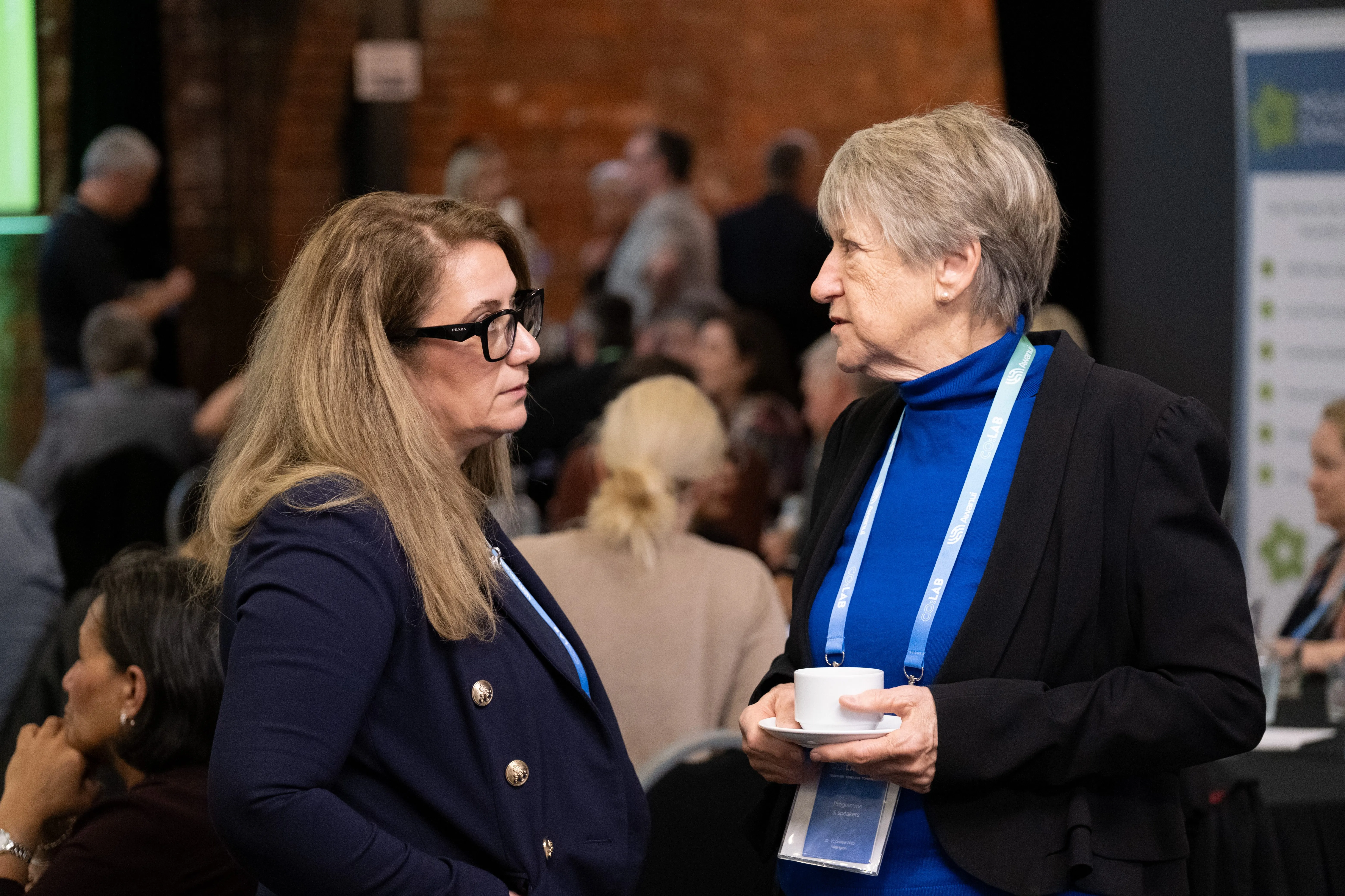 Two women in conversation at an Co:Lab with people in background