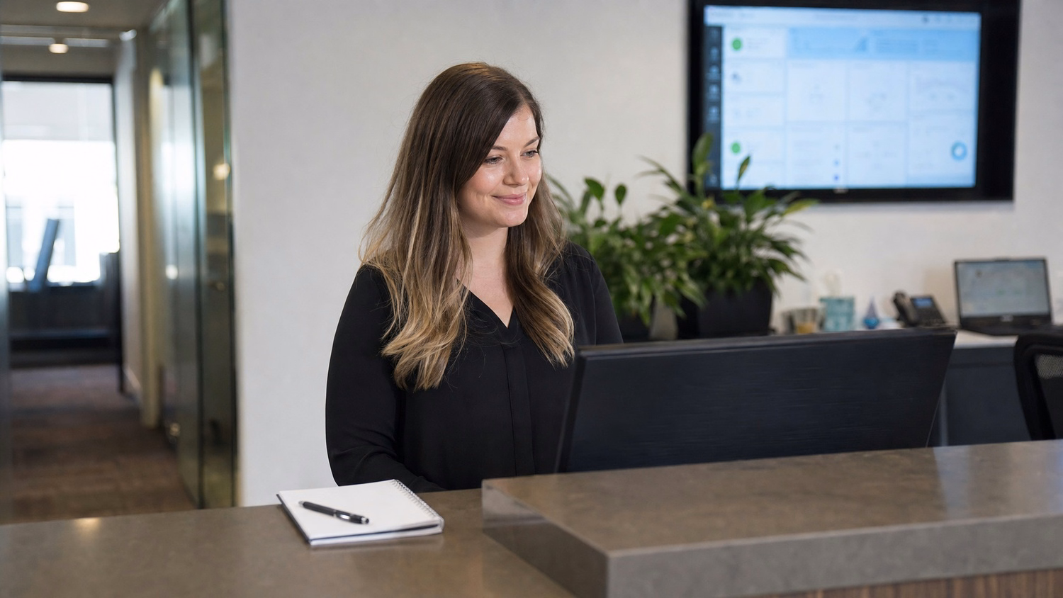 Receptionist at desk reviewing computer screen, office lobby
