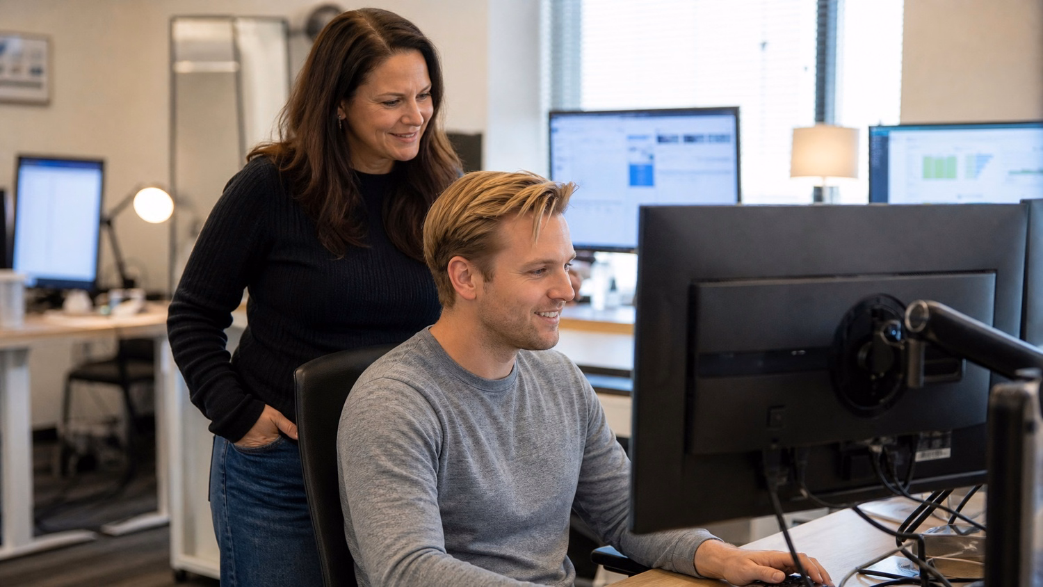Woman stands behind colleague, both look at screen 58