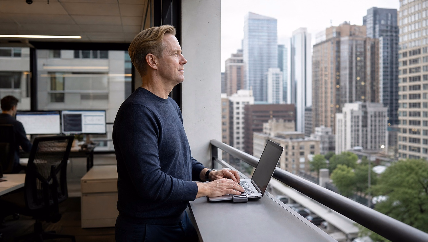Man on balcony reviewing laptop documentation