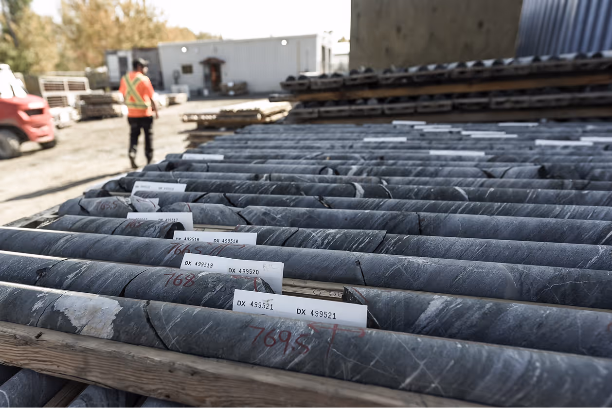 Rows of labeled cylindrical rock core samples laid out in an outdoor industrial site with a worker in safety vest.