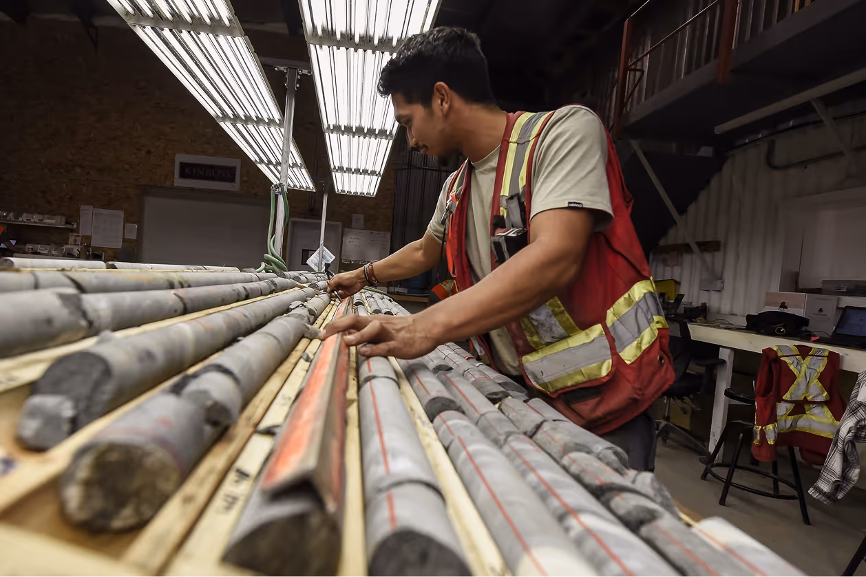 Worker in a red safety vest inspecting core samples laid out on a wooden table indoors.