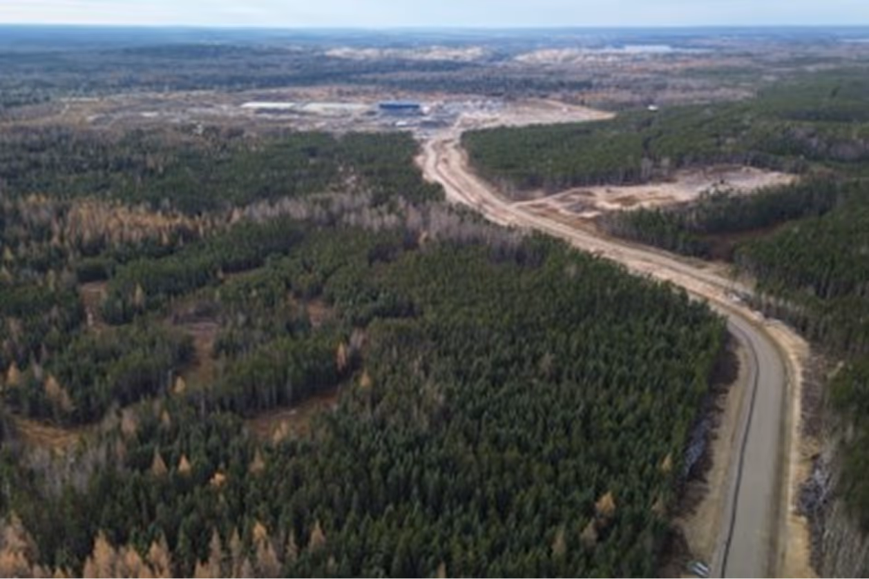 Aerial view of green forest with a winding road leading to a construction site in the distance.