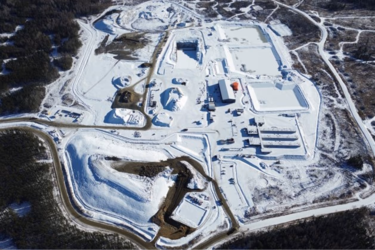Aerial view of an industrial mining site covered in snow, surrounded by forested land.