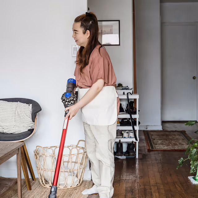 Woman using a cordless vacuum cleaner to clean a hardwood floor in a living room.
