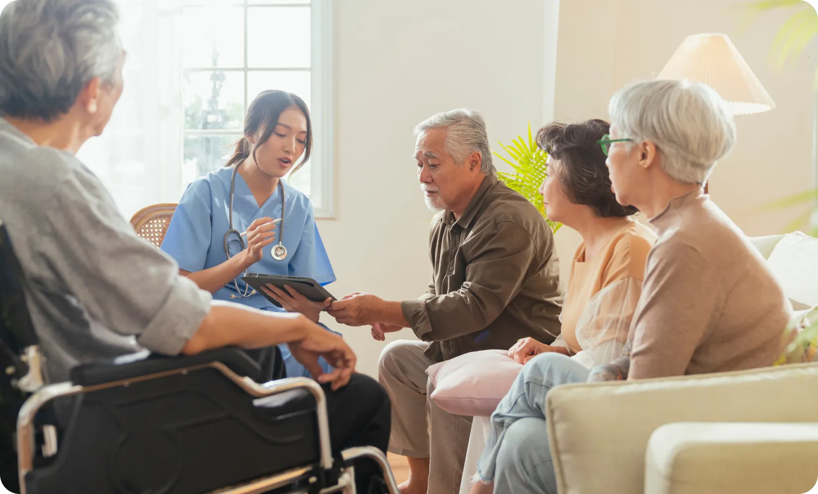 Young nurse in scrubs showing tablet to a group of senior adults in a living room.