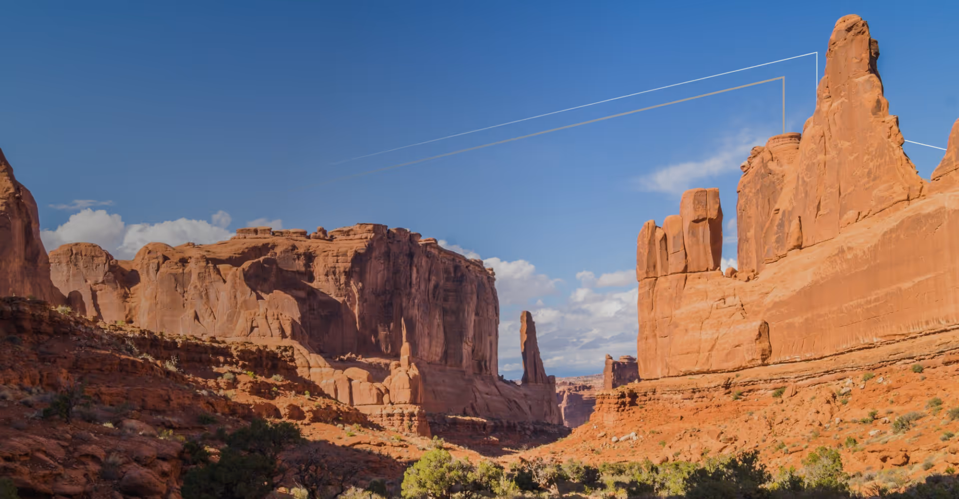 Arizona red rock formations under a blue sky with scattered clouds and sparse desert vegetation.