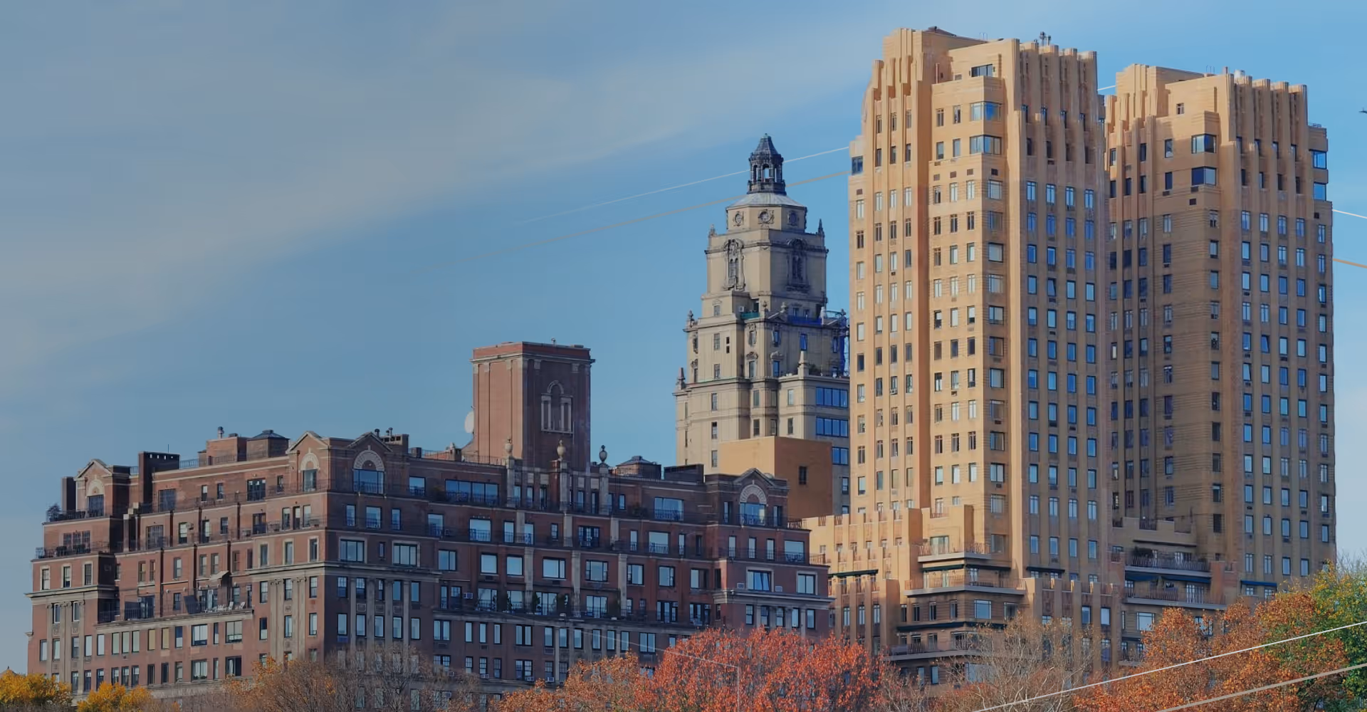 Tall historic buildings in a city skyline with clear blue sky and autumn trees in foreground.