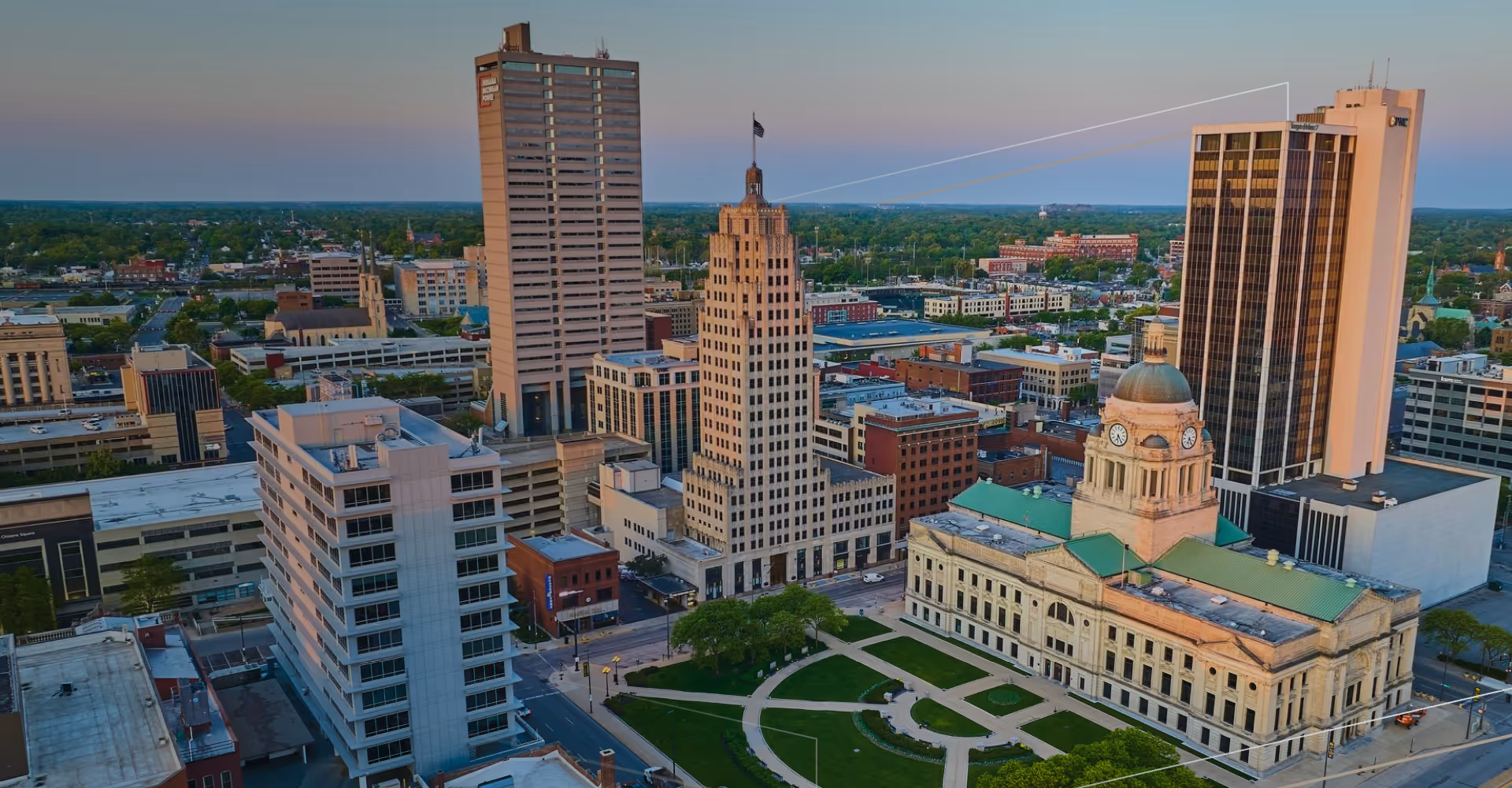 Downtown cityscape with a historic clock tower building and modern skyscrapers at sunset.