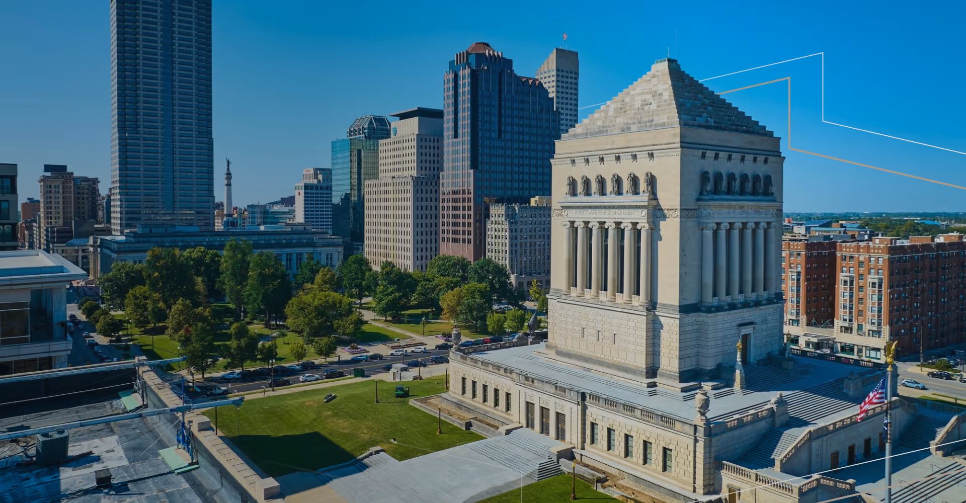 Downtown cityscape with a large monument building and surrounding green park under a clear blue sky.