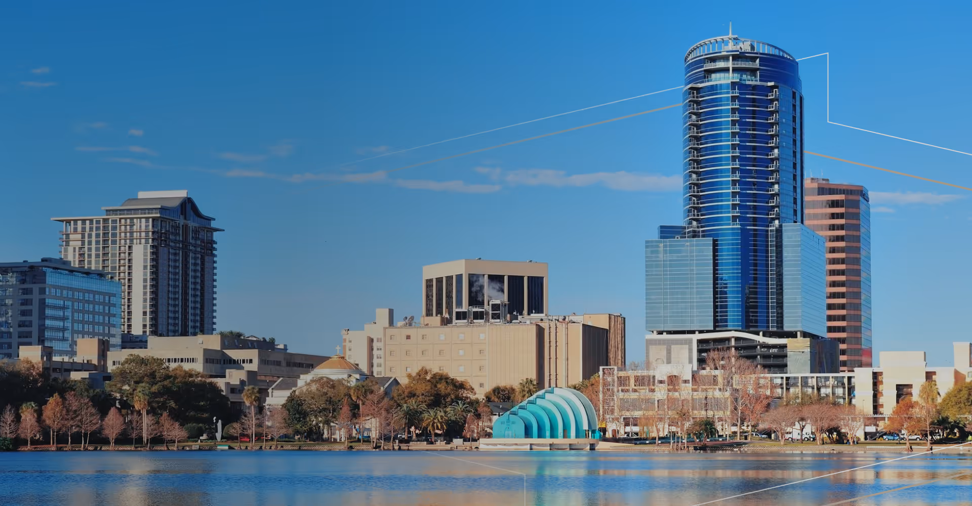 City skyline with modern and traditional buildings reflected in calm water under a clear blue sky.