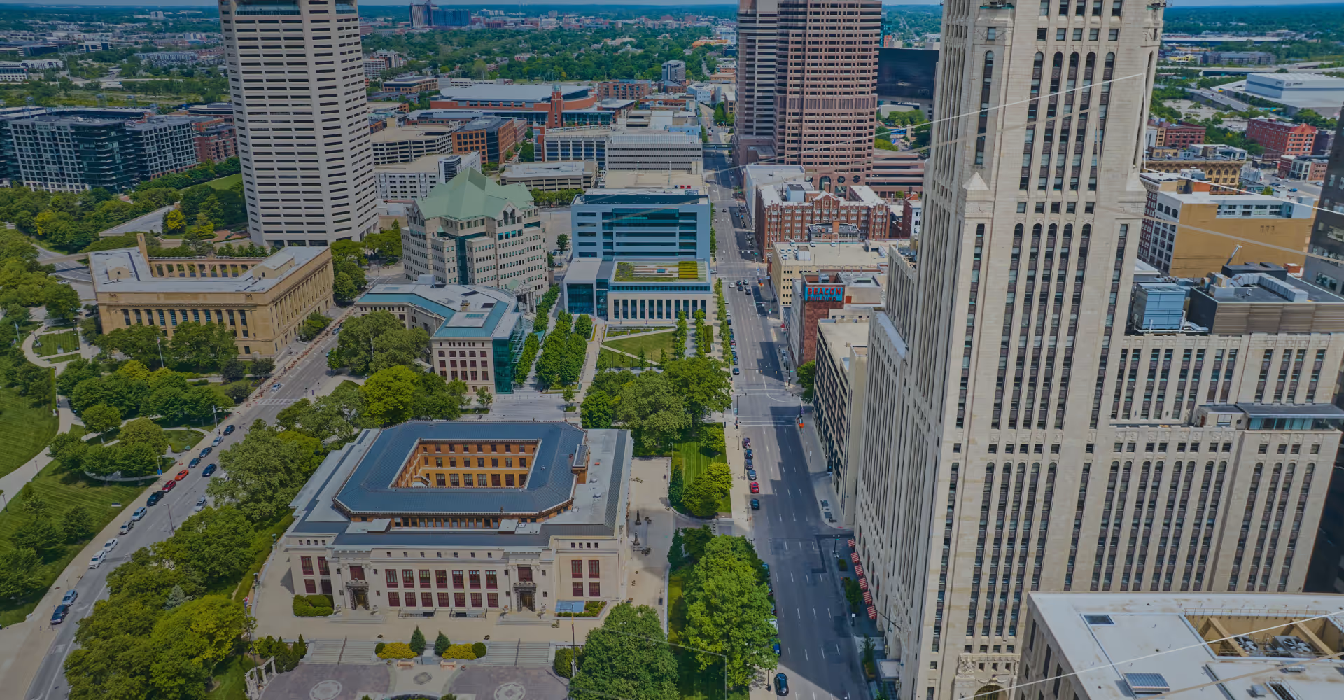 Aerial view of a cityscape with tall buildings, streets, and green parks in daytime.
